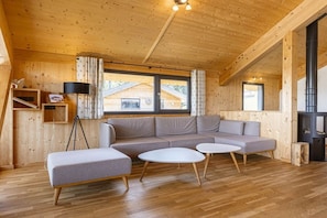 A cozy cabin interior with a wooden ceiling, a sofa set, a lamp, and a view of a wooden house outside. - Cabin in Pichl near Schladming with sauna (Pichl bei Schladming)