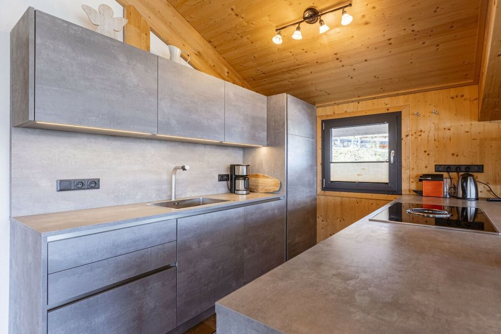 A modern kitchen with grey cabinets, a wooden countertop, and a window with a view.