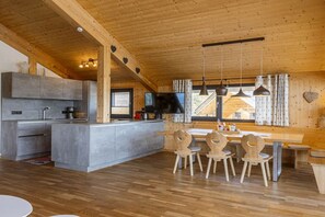 Una cocina moderna con una isla central, mesa de comedor de madera con sillas y un ventanal con cortinas.