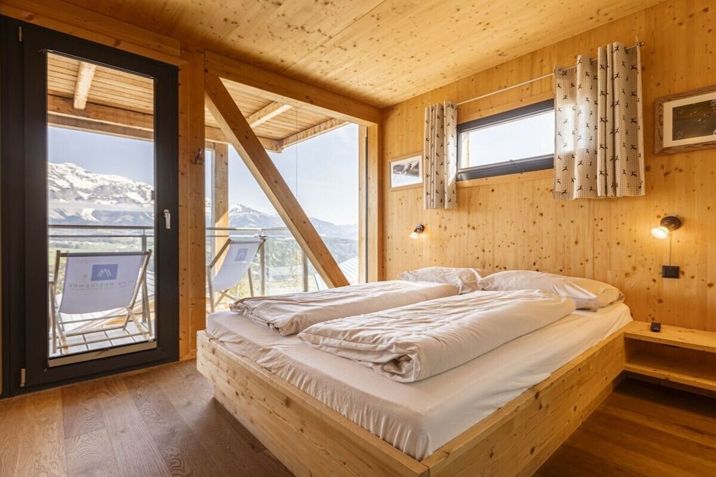Eine Holzhütte mit Bett, einem Vorhangfenster und Bergblick.