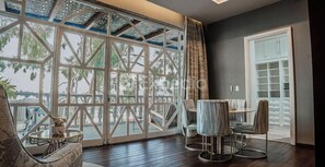 Un balcon donnant sur des arbres et un immeuble, un coin repas avec une table et des chaises, et une grande fenêtre avec un cadre en métal.