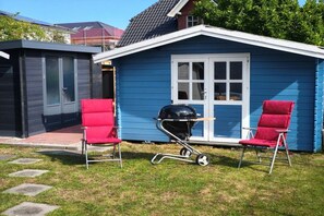 Et blåt hus med dør og vinduer, to røde stole, en grill og et mindre udhus.