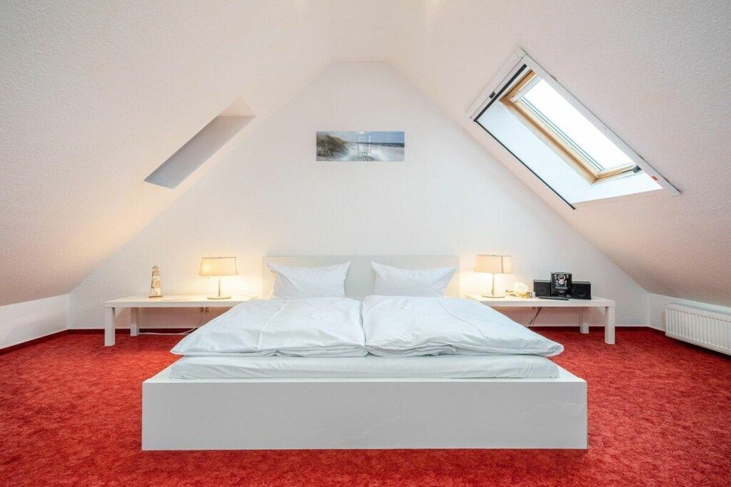 Une chambre avec un plafond en pente, un lit, deux tables de chevet avec des lampes, un petit tableau au mur et un puits de lumière.