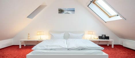 A bedroom with a sloped ceiling, a bed, two bedside tables with lamps, a small picture on the wall, and a skylight.