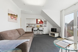 A modern living space with a sofa, a glass table, and a kitchen area in the background. - Ohana holiday apartment (Zingst (Ostseeheilbad))