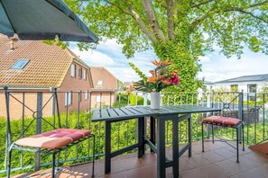 An outdoor patio with a table and two chairs, surrounded by a metal fence, with a tree and a flower arrangement in the background. - Ohana holiday apartment (Zingst (Ostseeheilbad))