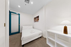 Een slaapkamer met een bed, een witte nachtkastje, een blauwe deur en een wandlamp.
