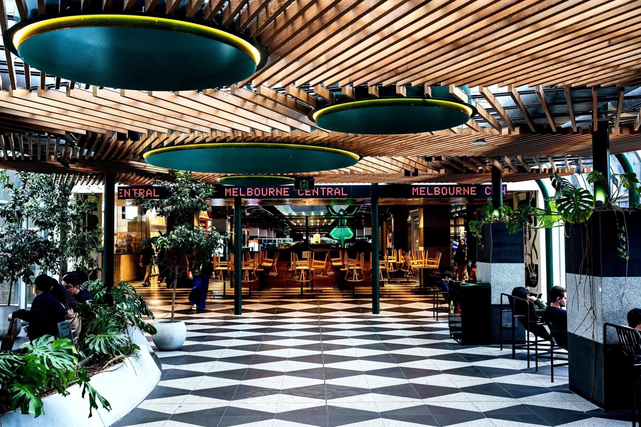 A spacious indoor area with a checkered floor, wooden ceiling, and hanging green circular lights.