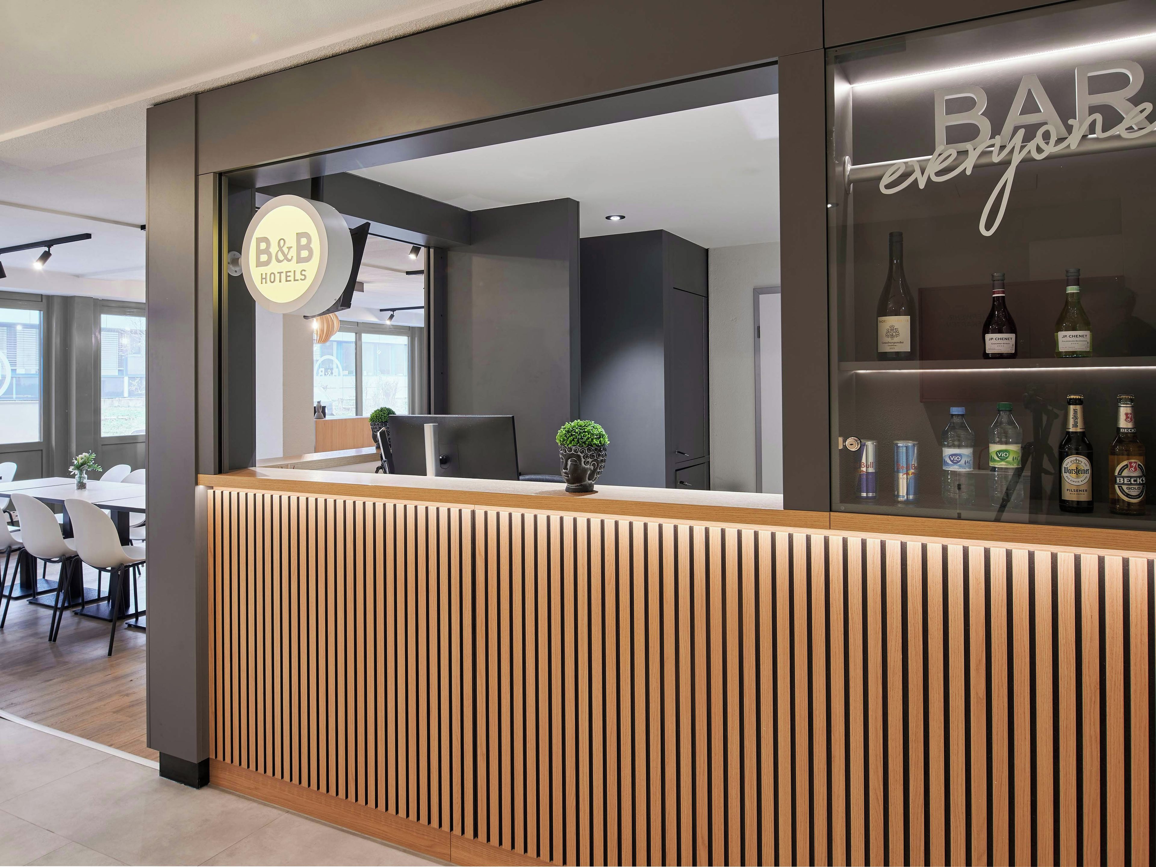 Una recepción con el letrero de B&B Hotels, una zona de bar con varias botellas y un diseño interior moderno.
