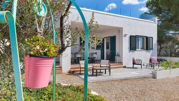 A modern house with a patio area, outdoor furniture, and a garden with potted plants.