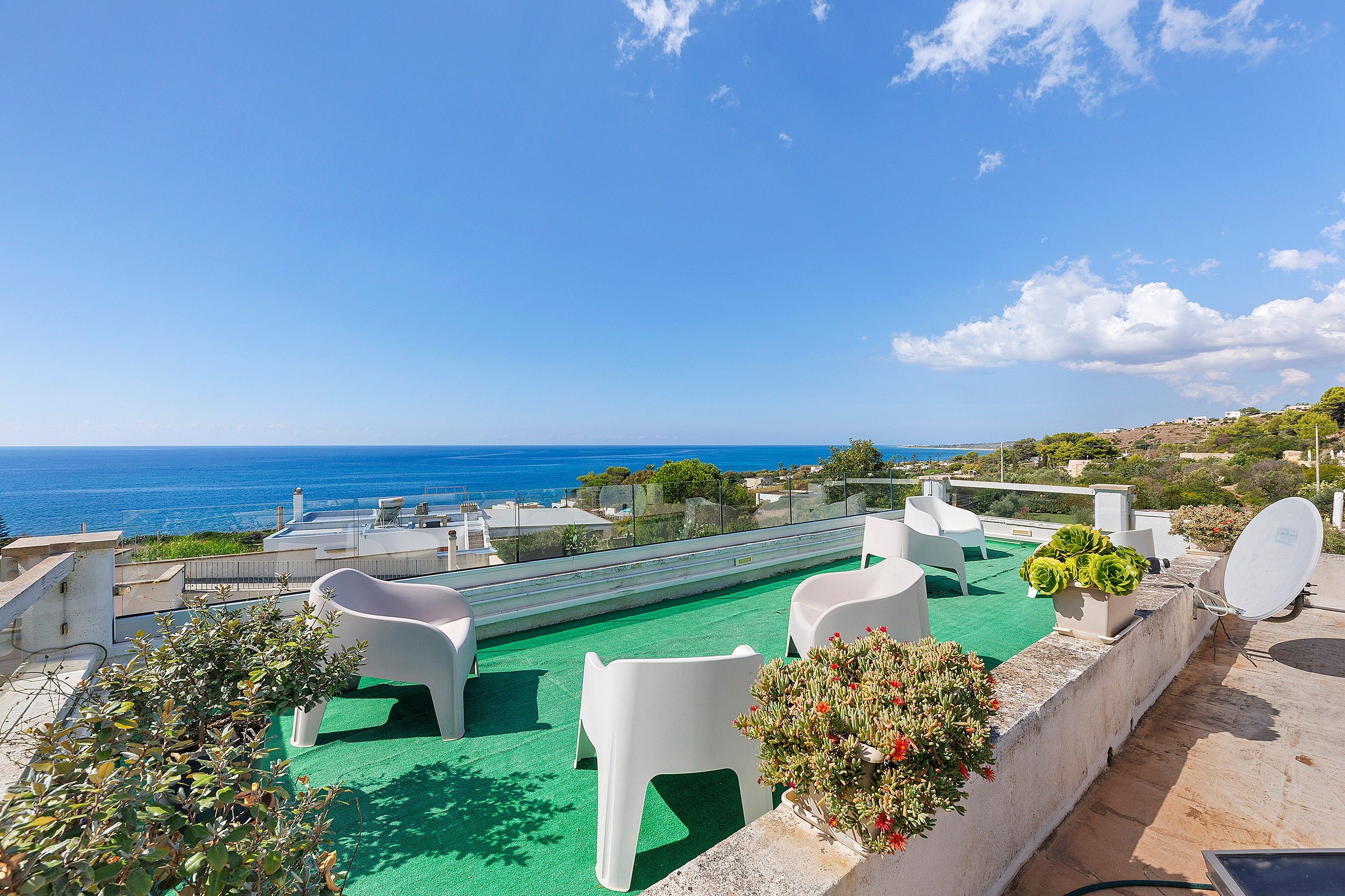 A rooftop terrace with a view of the sea, outdoor seating, and a satellite dish.