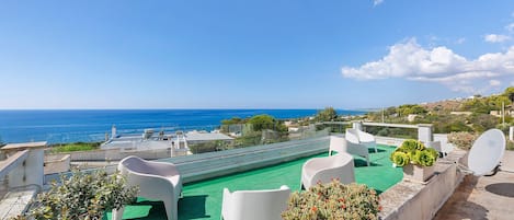 A rooftop terrace with a view of the sea, outdoor seating, and a satellite dish.