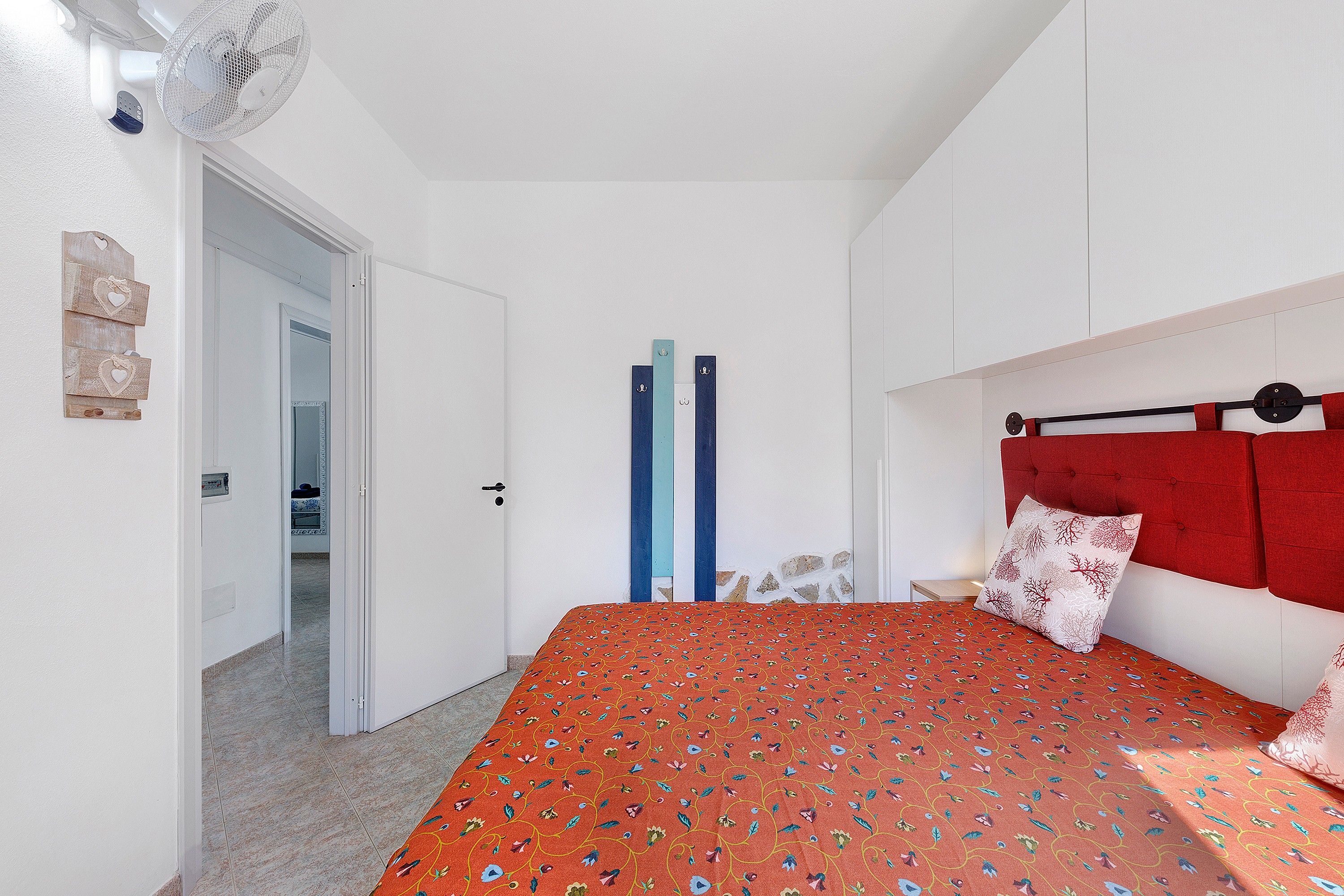 Ein Schlafzimmer mit einem Bett, einem roten Kopfteil, einer weißen Wand und einer Tür zu einem anderen Raum.