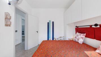 Ein Schlafzimmer mit einem Bett, einem roten Kopfteil, einer weißen Wand und einer Tür zu einem anderen Raum.