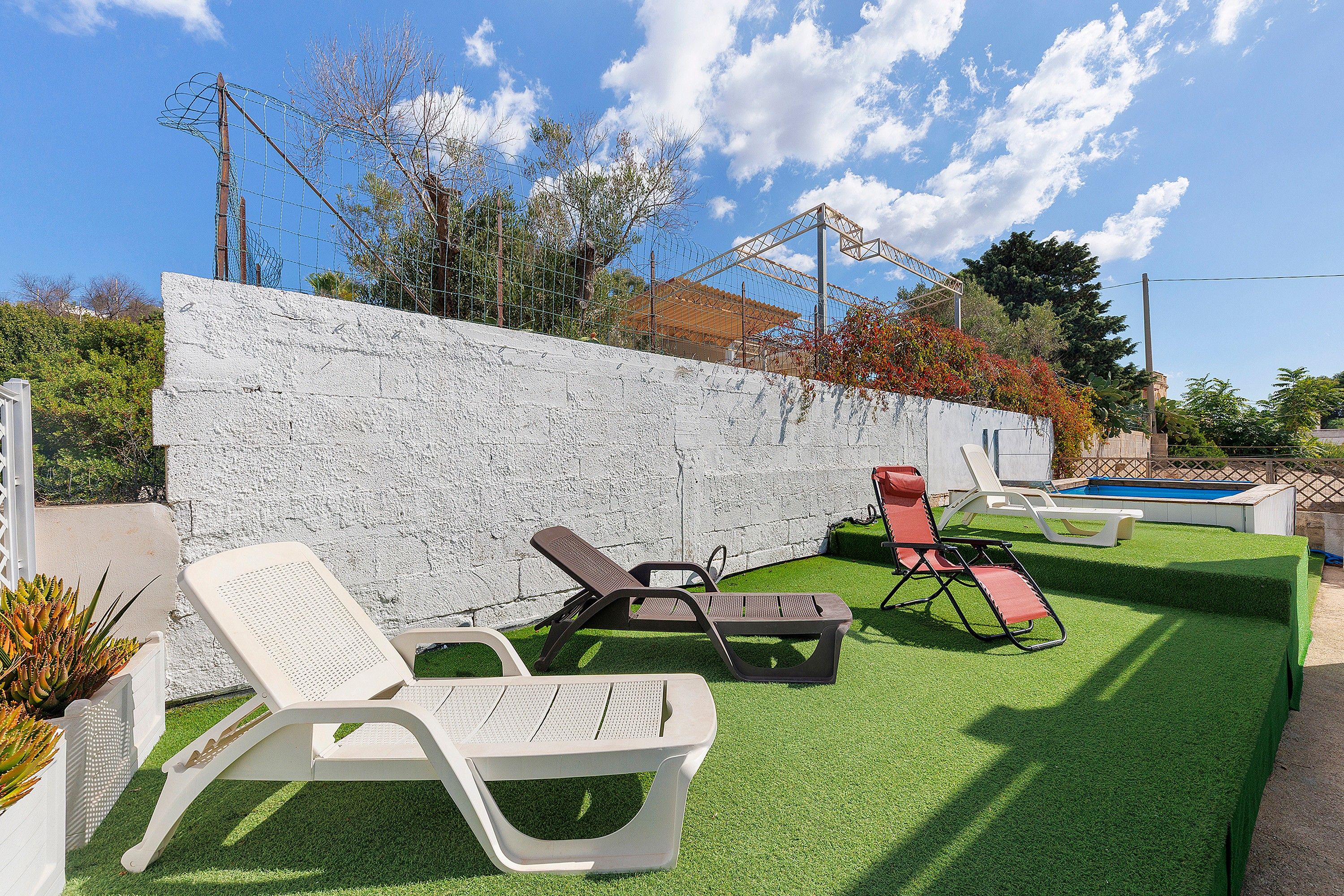 Ein Garten mit Kunstgrasanlage, einer weißen Wand und mehreren Liegestühlen.