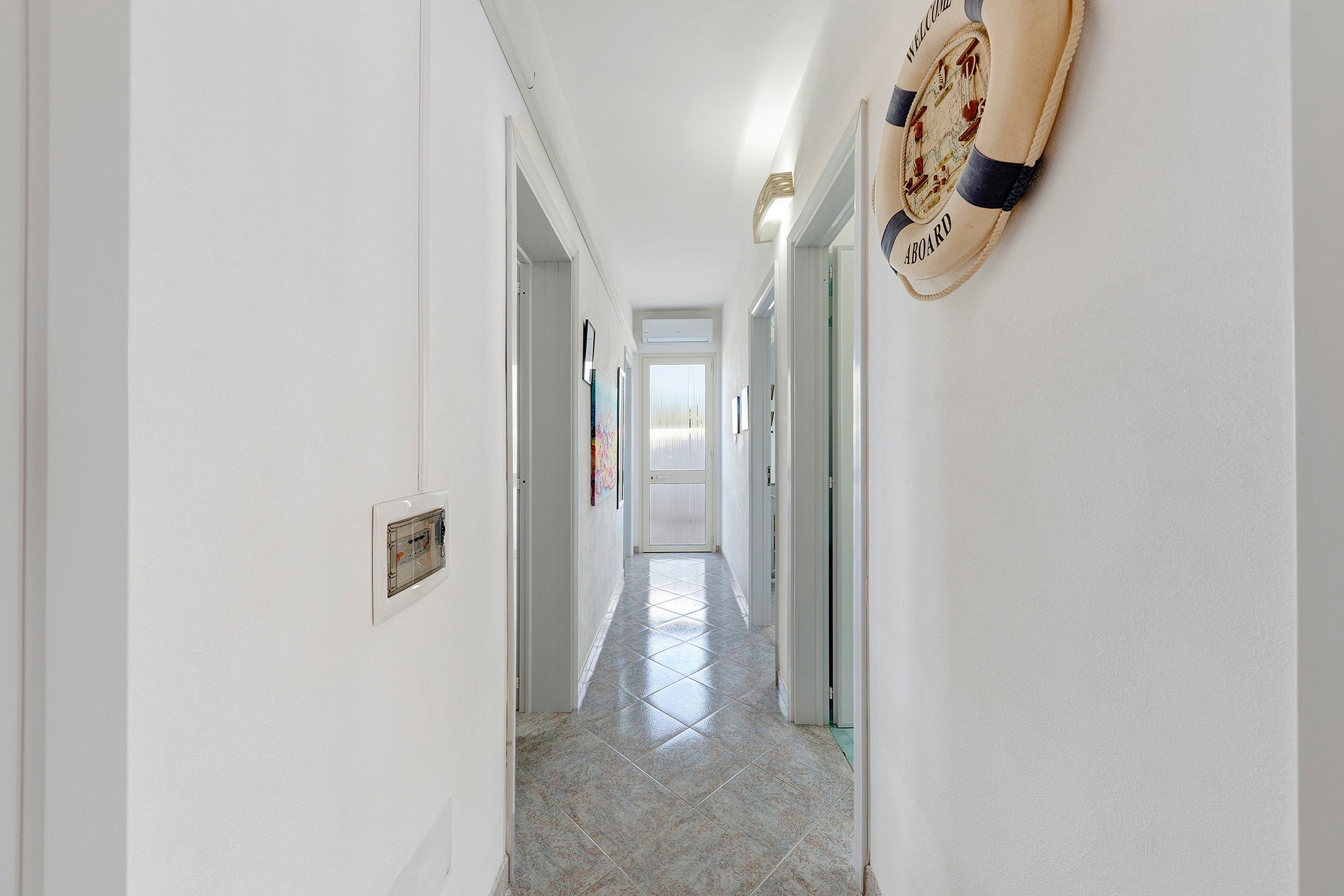 A hallway with a tiled floor, white walls, and a door at the end.
