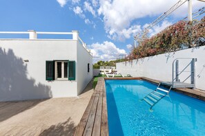 Ein Schwimmbecken mit Holzterrasse und einem Gebäude mit Fensterläden.