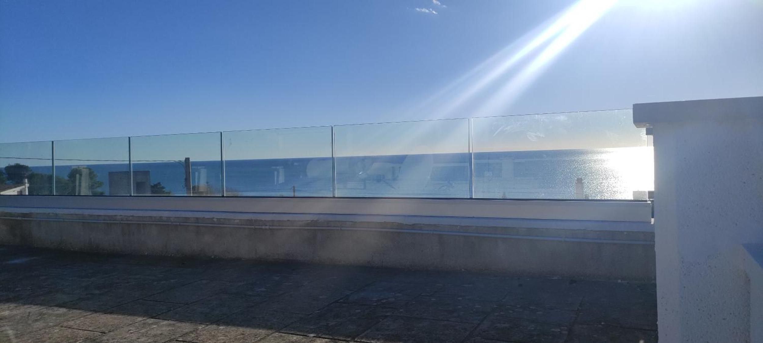 A clear sky with the sun shining, a reflective glass barrier, and a body of water in the background.