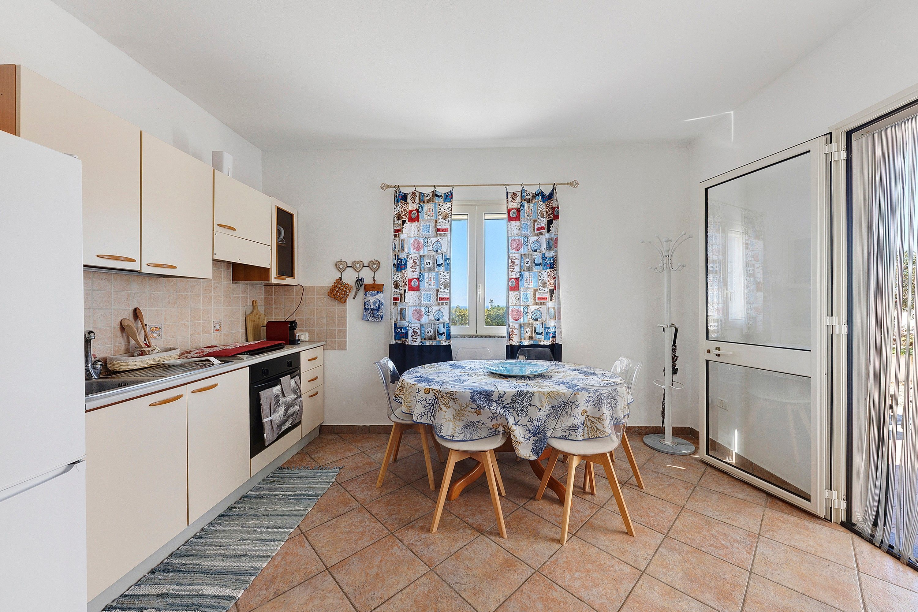 Une cuisine compacte avec un coin repas, dotée d’un sol carrelé, de meubles en bois et d’une table dressée pour quatre personnes.