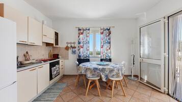 Une cuisine compacte avec un coin repas, dotée d’un sol carrelé, de meubles en bois et d’une table dressée pour quatre personnes.