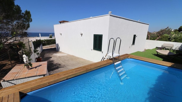 A swimming pool with a wooden deck, a white building with two doors, and a view of the sea. - Villa 'Stella' with Sea View, Wi-Fi and Air Conditioning (Torre Vado)