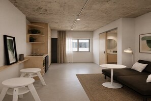 A modern living room with a sofa, two white tables, a kitchen area with a sink, and a large window. - Studio in Darwin CBD with Coffee Setup (Darwin City)