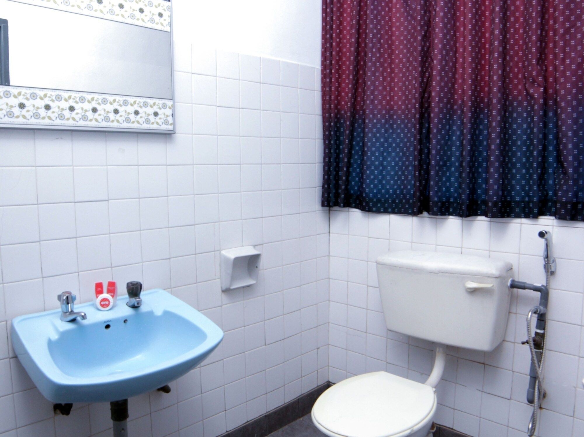 A bathroom with a white toilet, a blue sink, and a mirror with a floral border.