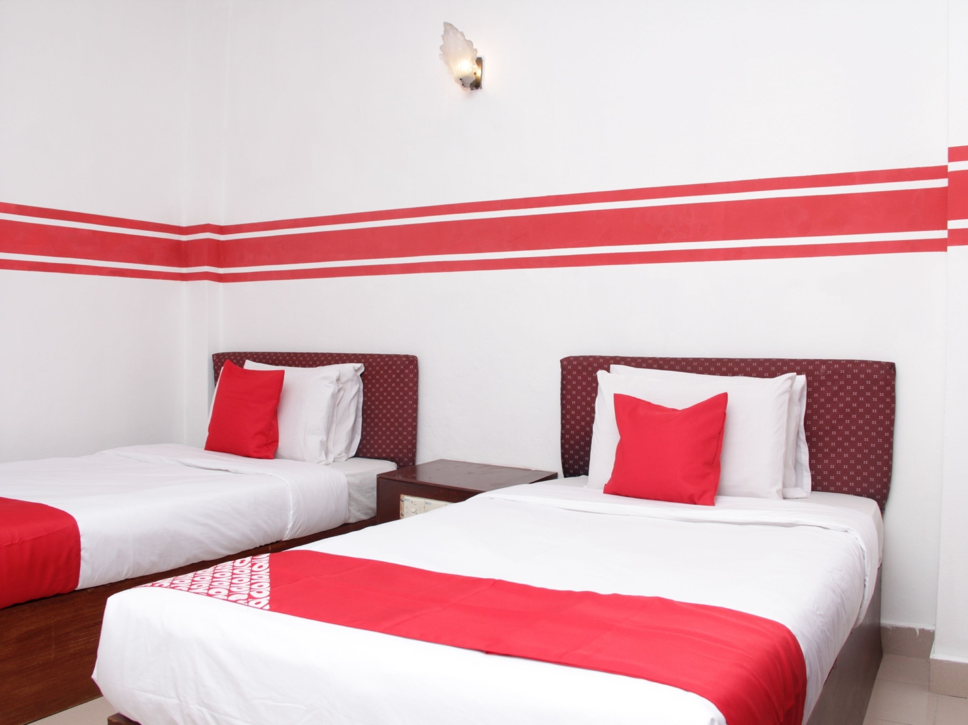 A hotel room with two beds, each with a red and white bedspread, and a red accent wall.