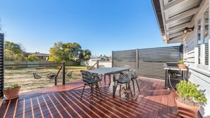 Une terrasse en bois avec une table et des chaises, un barbecue et des plantes en pot.