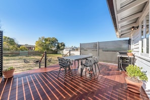 A wooden deck with a table and chairs, a barbecue grill, and potted plants.