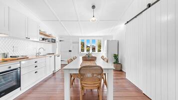 A modern kitchen with white cabinetry, a wooden countertop, and a dining area with a white table and wicker chairs.