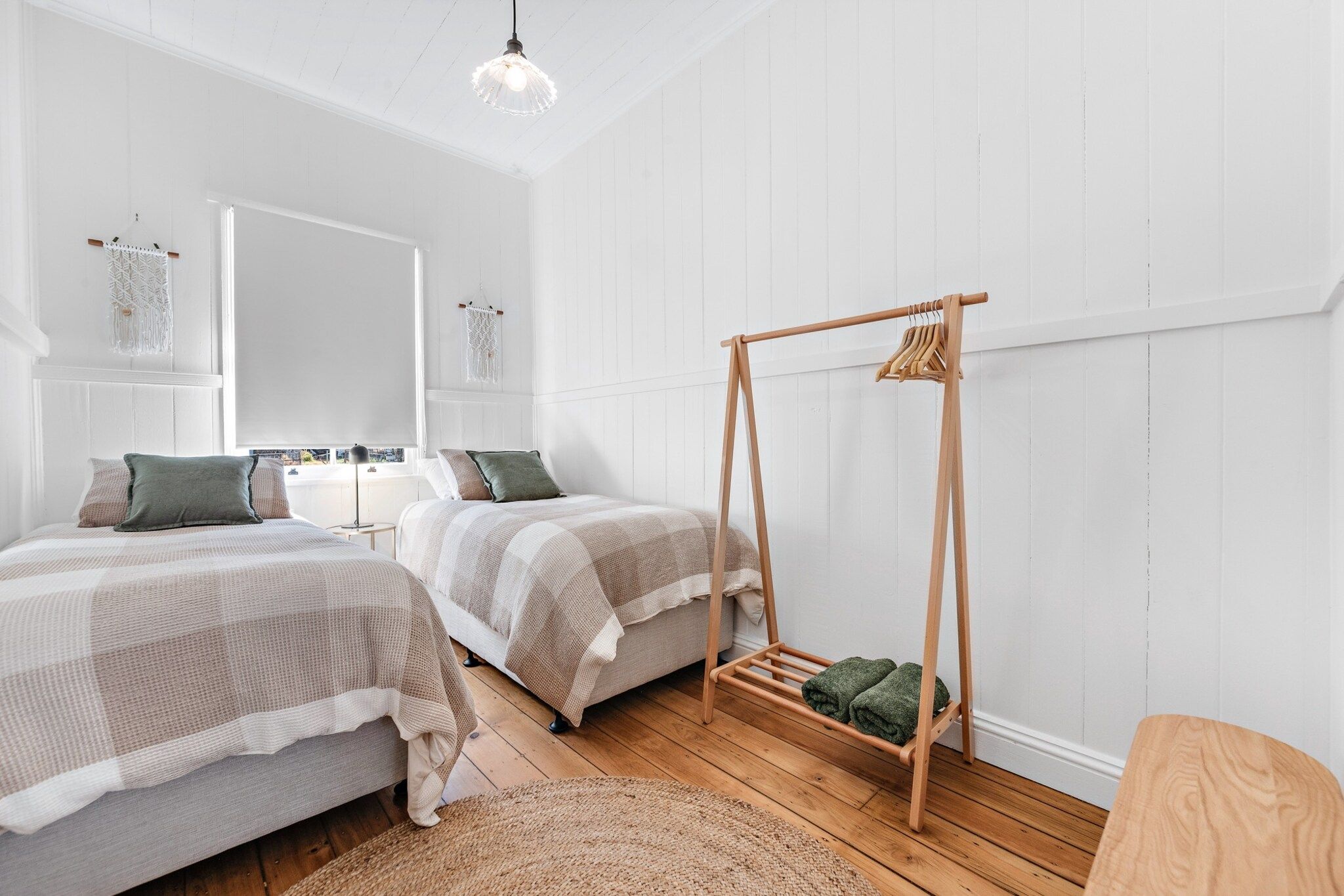 A bedroom with two beds, a wooden swing chair, and a large mirror.