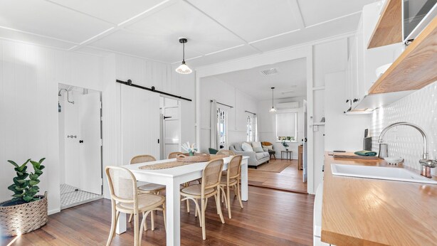 Une cuisine moderne avec des meubles blancs, un plan de travail en bois et un coin repas doté de chaises en osier.