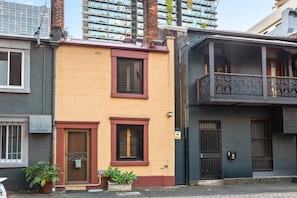 A two-story building with a flat facade, a small balcony on the second floor, and a door with a metal gate. - Stylish 2-Bed House Near Sydney CBD (Chippendale)