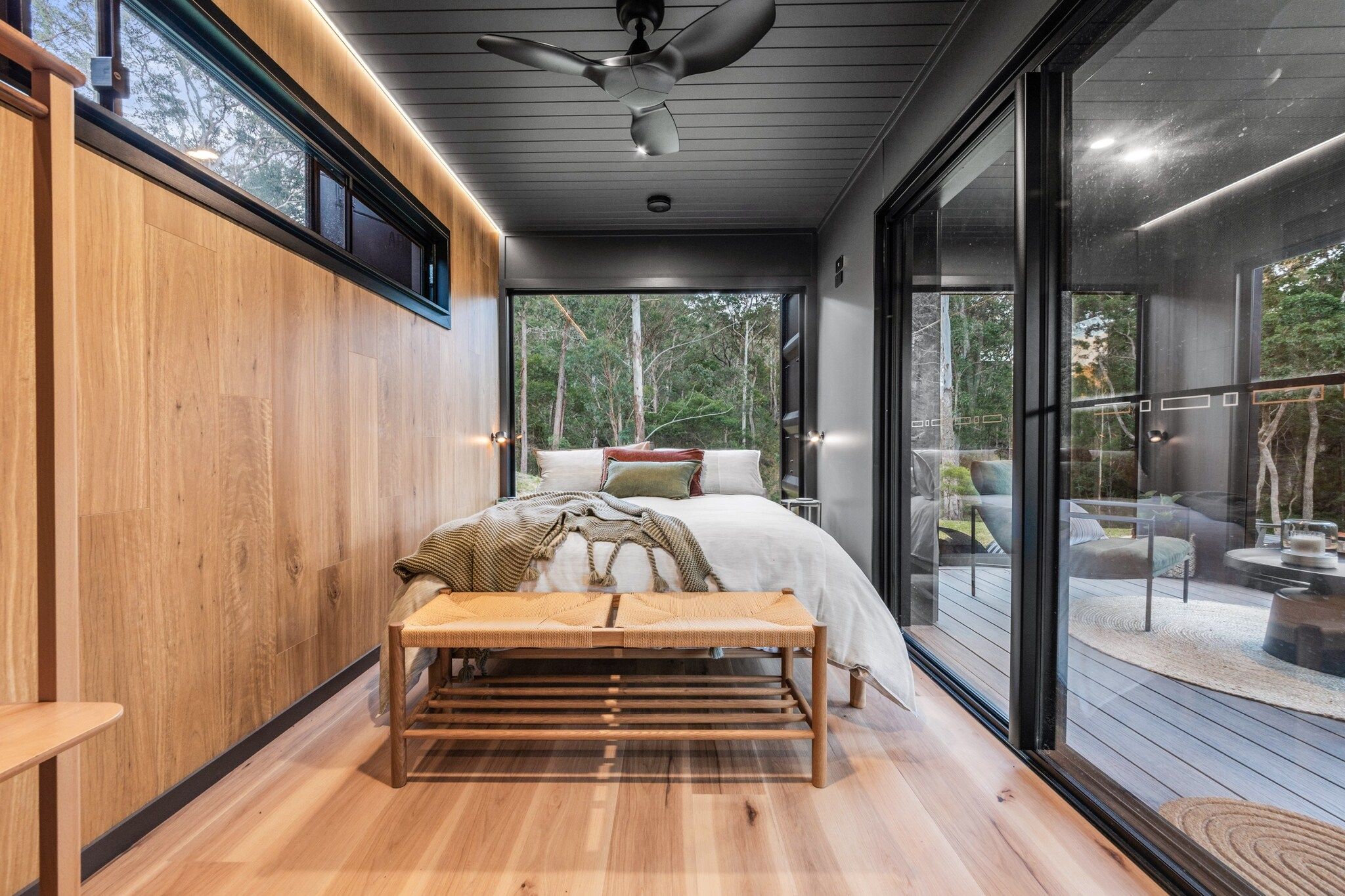 A bedroom with a bed, bench, and large windows.