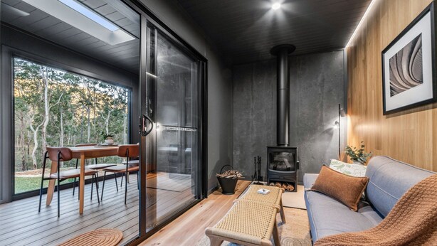 A modern interior with a sofa, a table, and a wooden deck. - Mijo | The Nook-Off grid Rural Retreat (Tenterfield)