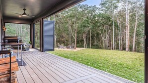 An outdoor deck with a grill and seating area, overlooking a grassy yard and forest. - Mijo | The Nook-Off grid Rural Retreat (Tenterfield)