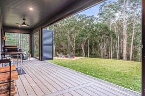 An outdoor deck with a grill and seating area, overlooking a grassy yard and forest.