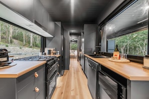 A modern kitchen with a central island, wooden countertops, and a view of a forested area.
