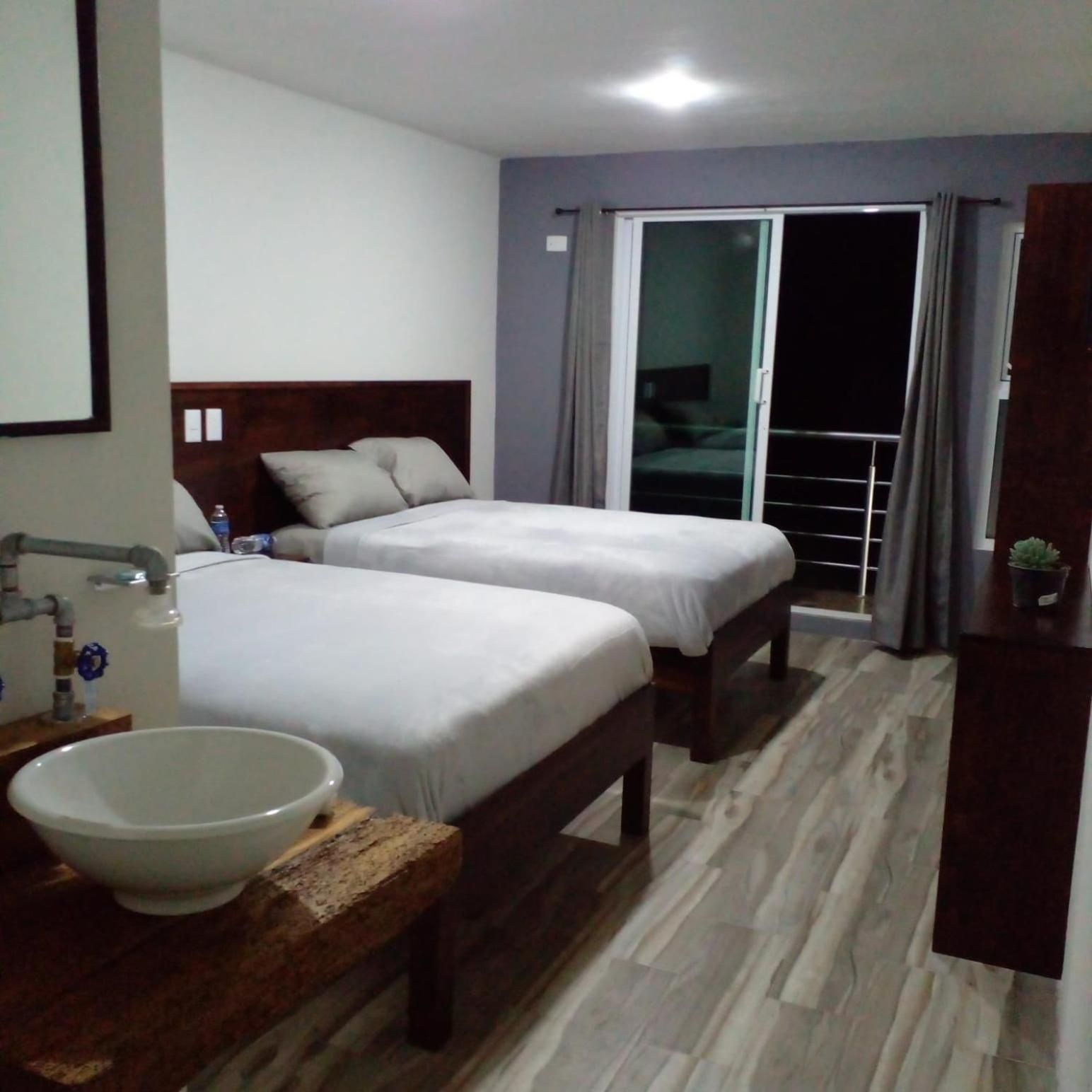 Habitación de hotel con dos camas, baño con lavabo y espejo, y balcón con vistas.