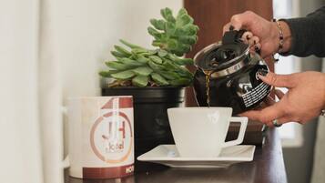 Una persona sirve café en una taza sobre una barra con una planta en maceta y una taza de hotel.