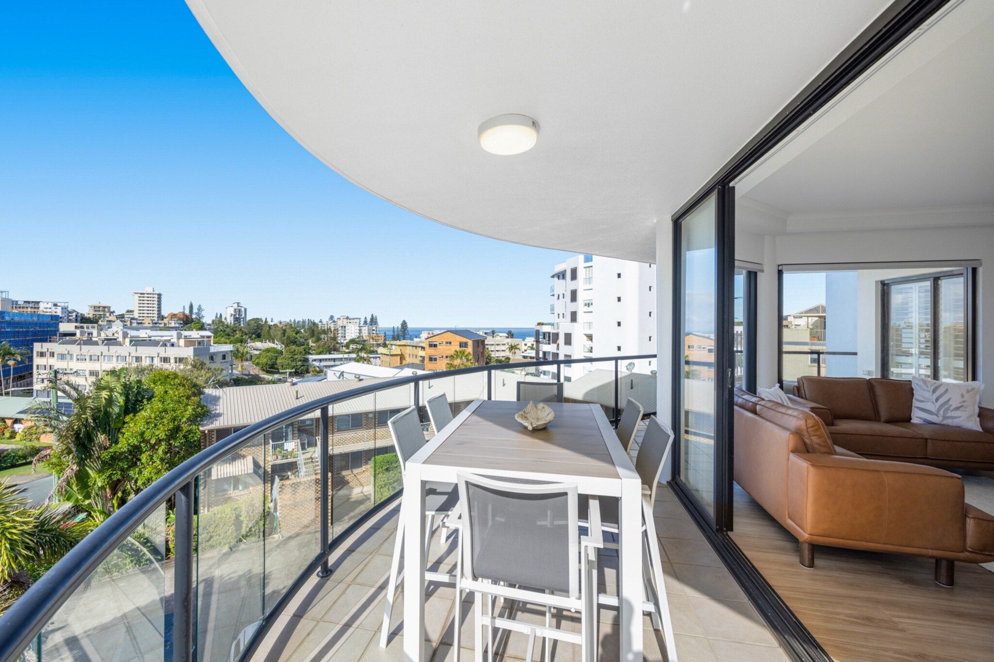A balcony with a dining table and chairs, a sofa, and a view of the cityscape.
