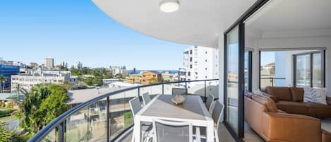 A balcony with a dining table and chairs, a sofa, and a view of the cityscape.