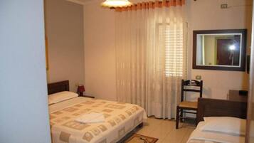 A hotel room with a bed, a chair, a desk, a mirror, and a window with curtains.