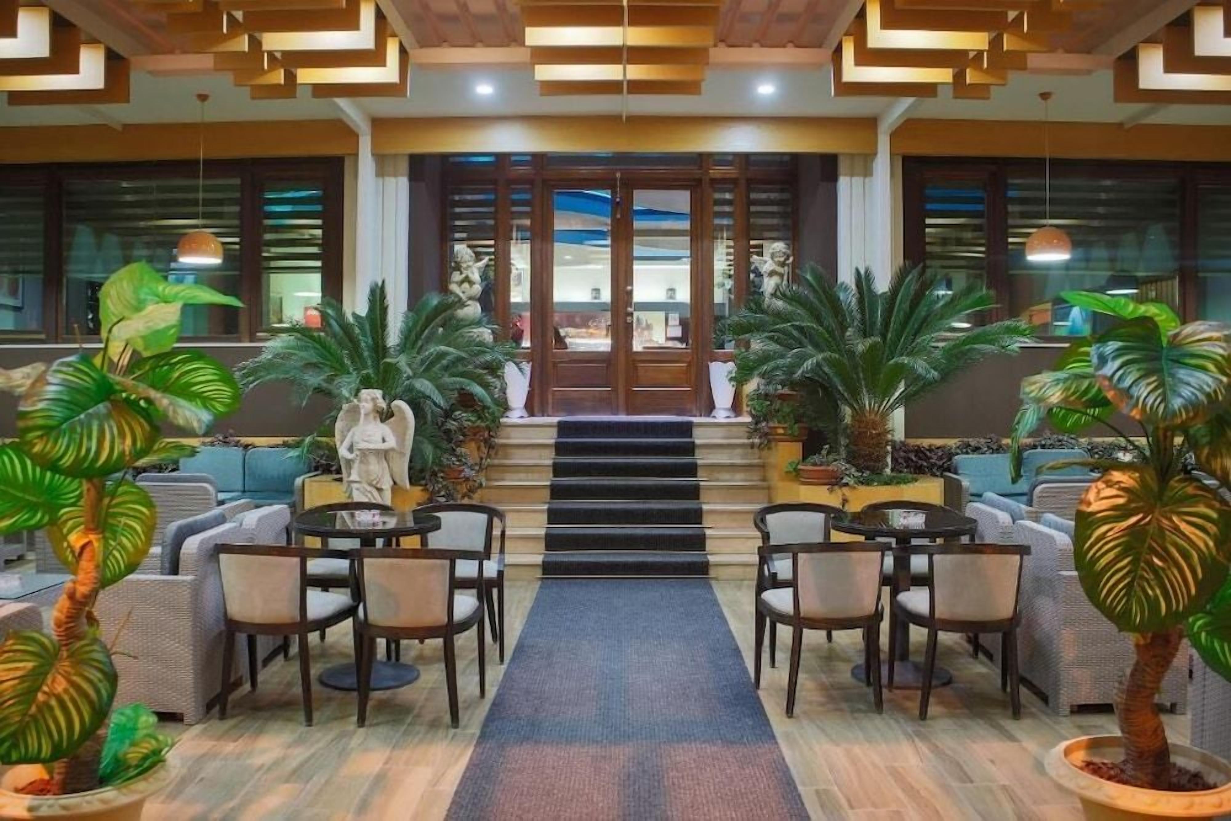 A lobby with a central staircase, seating area, and potted plants.