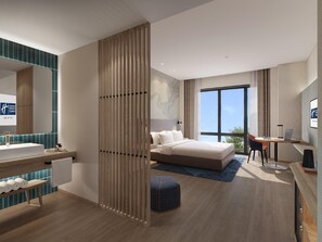 Une chambre d’hôtel moderne dotée d’un grand lit, d’un bureau, d’un ordinateur portable, d’une salle de bain avec un lavabo et un miroir, et offrant une vue sur le ciel.