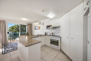 A modern kitchen with white cabinets, a central island, and a dining area with a view. - Charming 2-Bed Coastal Haven Near Esplanade (Maroochydore)