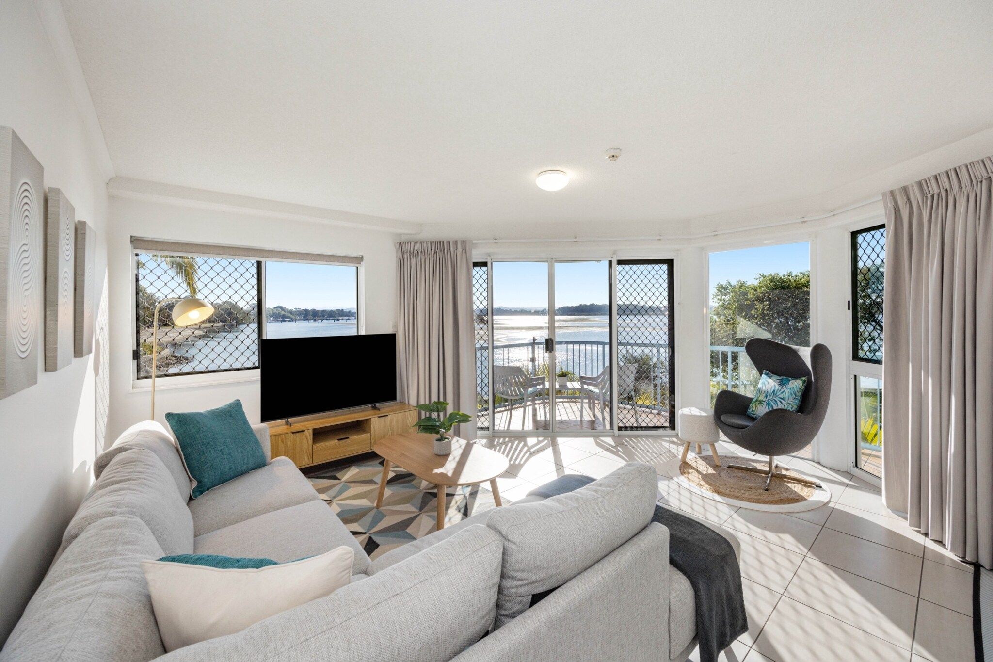 A modern living room with a sofa, TV, and a balcony with a view of the water.