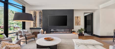 Una sala de estar moderna con un televisor de pantalla plana grande, chimenea y vistas al exterior.