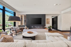 A modern living room with a large flat-screen TV, a fireplace, and a view of the outdoors. - Chateau Royale | One Snowmass East #605 | 4B/4B (Snowmass Village)